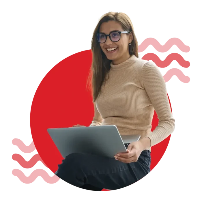 A young woman in business casual and glasses smiling while using a laptop